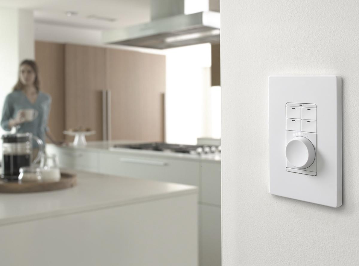 Savant Metro keypad installed on a wall in a modern kitchen, with a woman in the background holding a coffee mug.